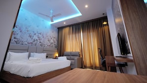 Una habitación de hotel moderna con cama, escritorio, silla, ventilador de techo y un ventanal con cortinas.