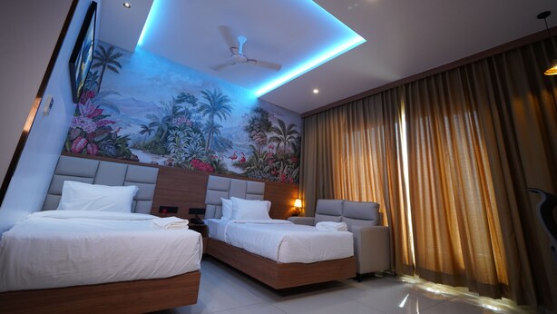 Habitación de hotel con dos camas, ventilador de techo, un mural y un ventanal con cortinas.
