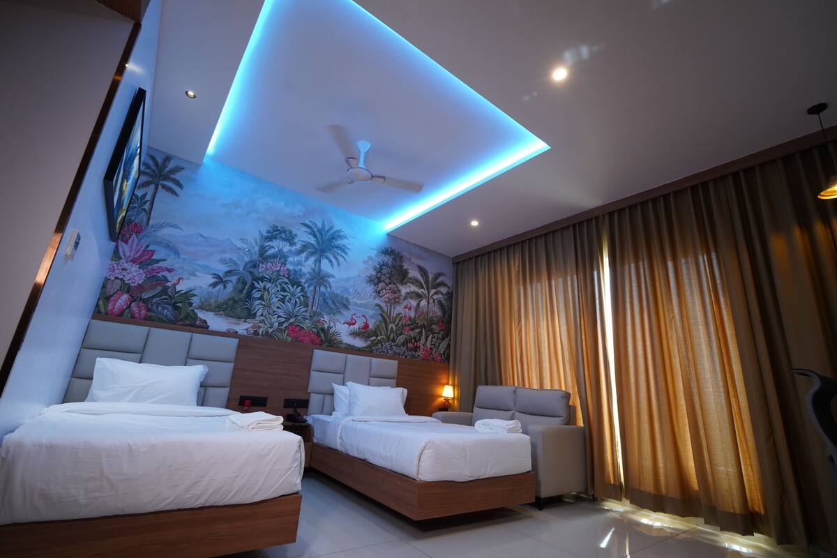 A hotel room with two beds, a ceiling fan, a mural, and a large window with curtains.