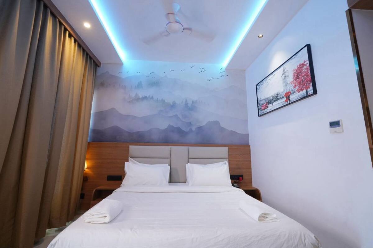 A hotel room with a bed, a ceiling fan, a mural on the wall, and a painting.