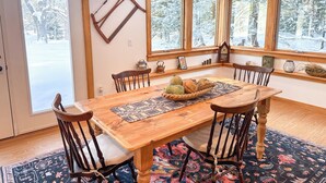 A dining room with a wooden table, six chairs, a large window with a view of a snowy landscape, and a rustic wall decor.
