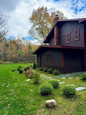 Une maison à deux étages, à l’extérieur sombre et aux bordures rouges, entourée d’une pelouse et d’un jardin bien entretenus.