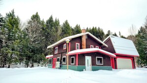 A two-story wooden house with a snow-covered roof and a red and white trim.