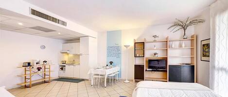 Habitación de hotel con dos camas, kitchenette, zona de comedor y televisor.