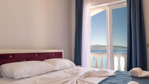 A hotel room with a bed, a view of the sea, and a balcony with curtains. - Erdano Hotel (Sarande)