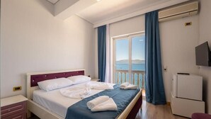 A hotel room with a bed, a desk, a TV, and a balcony with a view. - Erdano Hotel (Sarande)