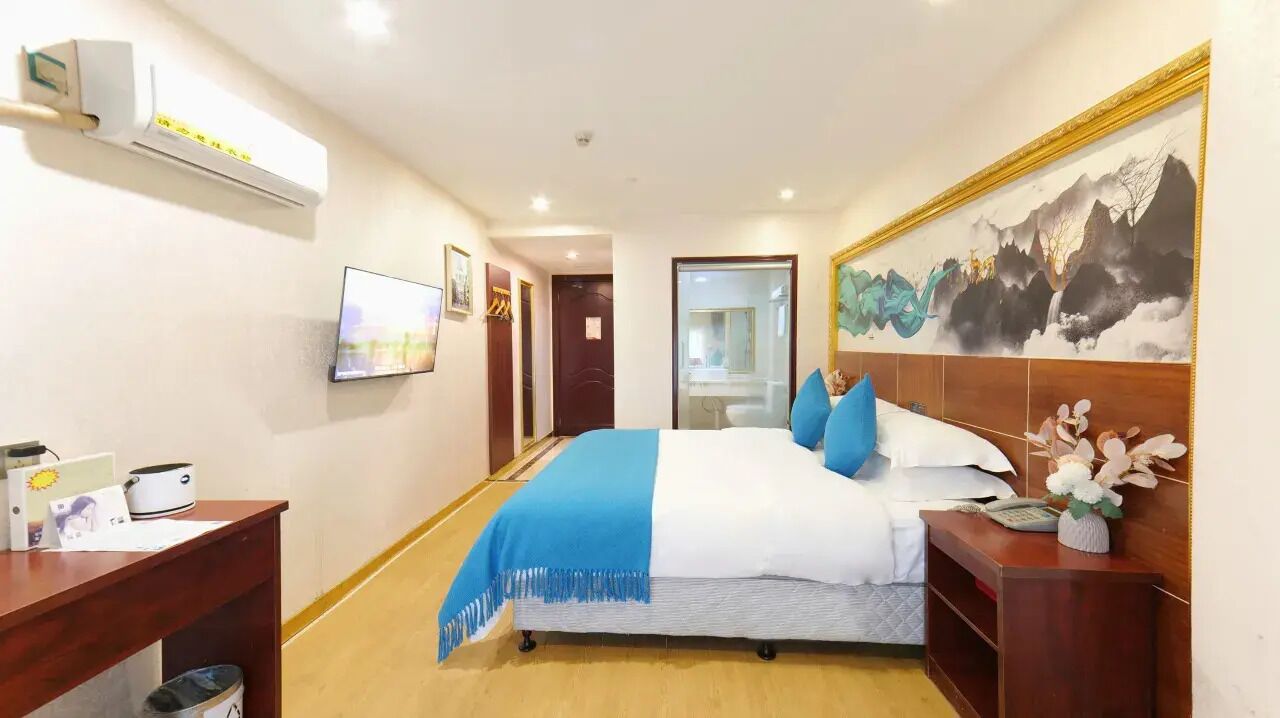 A hotel room with a bed, a TV, a desk, and a painting on the wall.