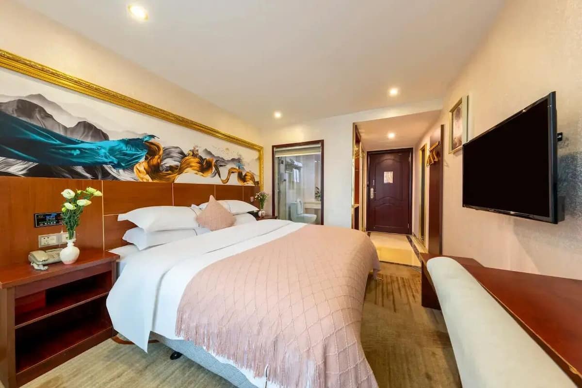 Hotelkamer met een bed, nachtkastje, televisie, kunstwerk aan de muur en een deur naar de badkamer.