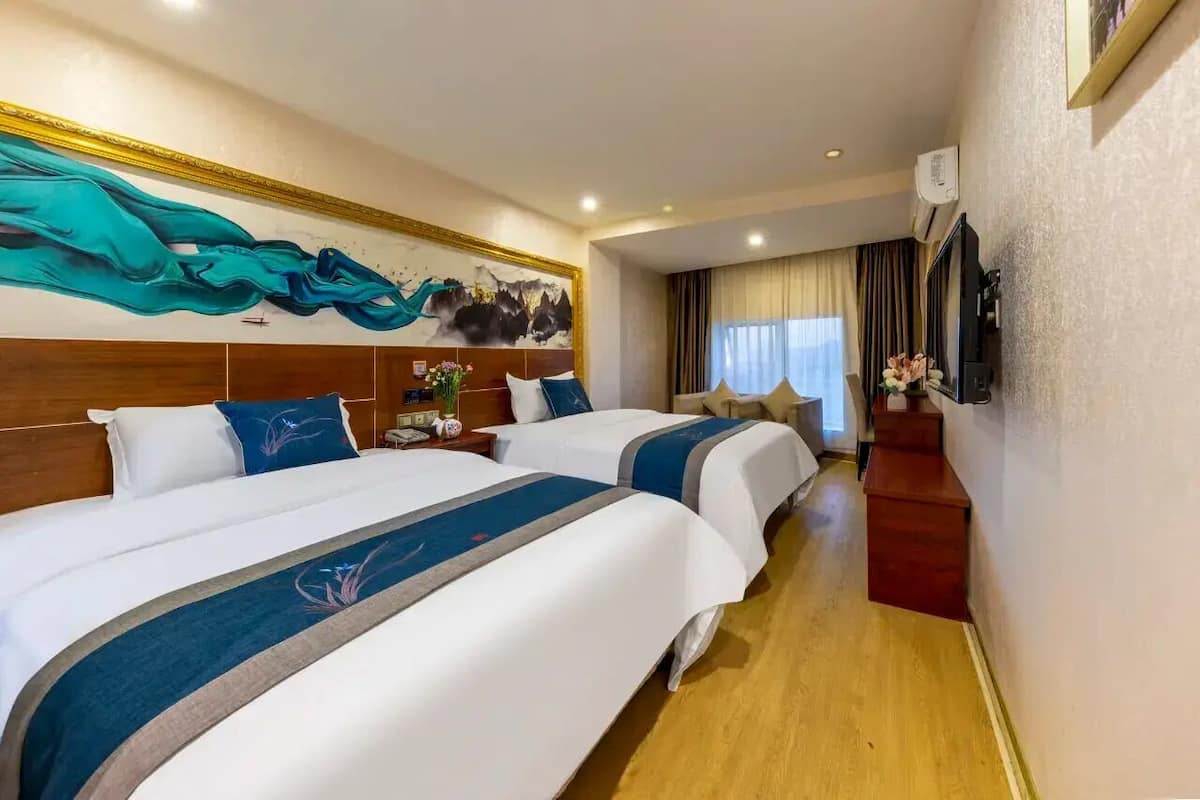 Een hotelkamer met twee bedden, een houten hoofdeinde, een schilderij, een televisie en een bureau met een bloevas.
