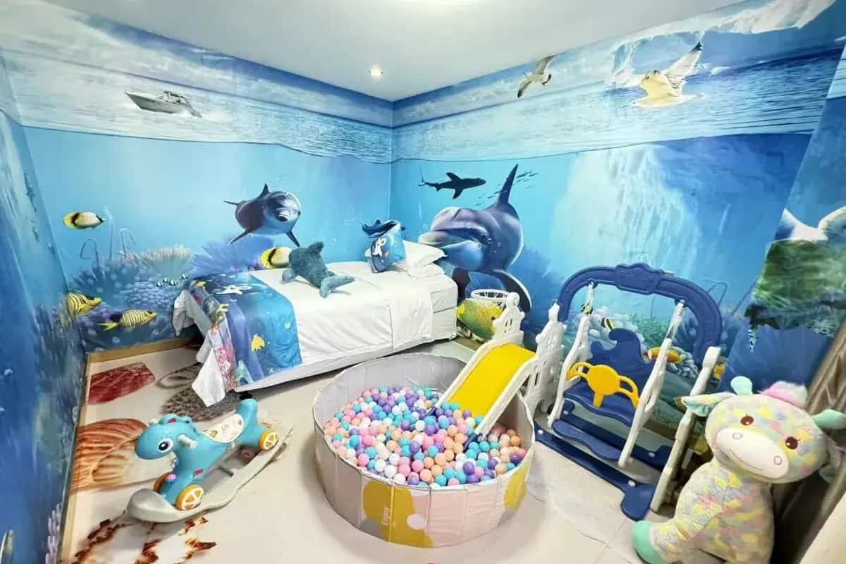 Een kamer met een muurschildering van een blauwe oceaan, een bed, een ballenbak en diverse speelgoed.