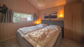 A wooden-paneled bedroom with a bed, a window with curtains, a bedside lamp, and a picture on the wall. - Vacation home Seebrise with sauna, fireplace & rowing boat and beach directly on the Dümmer See. (Dümmer)