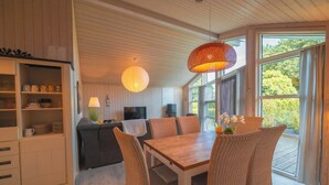 A modern living room with a dining table, wicker chairs, a sofa, and a television. - Vacation home Seebrise with sauna, fireplace & rowing boat and beach directly on the Dümmer See. (Dümmer)