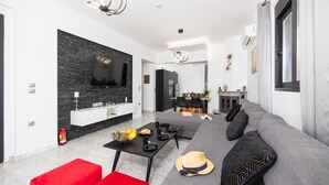 Un saló modern amb un sofà gris, un pouf vermell i una zona de menjador amb taula negra.
