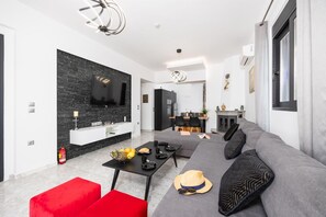 Ein modernes Wohnzimmer mit einem grauen Sofa, einem roten Hocker und einem Essbereich mit einem schwarzen Tisch.