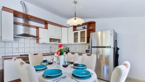 Una cocina moderna con armarios blancos, un refrigerador de acero inoxidable y una mesa de comedor para cuatro personas, con platos azules y sillas blancas.
