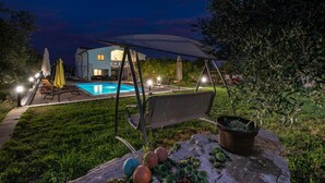 Un patio trasero con piscina, una silla colgante y una zona de estar techada.