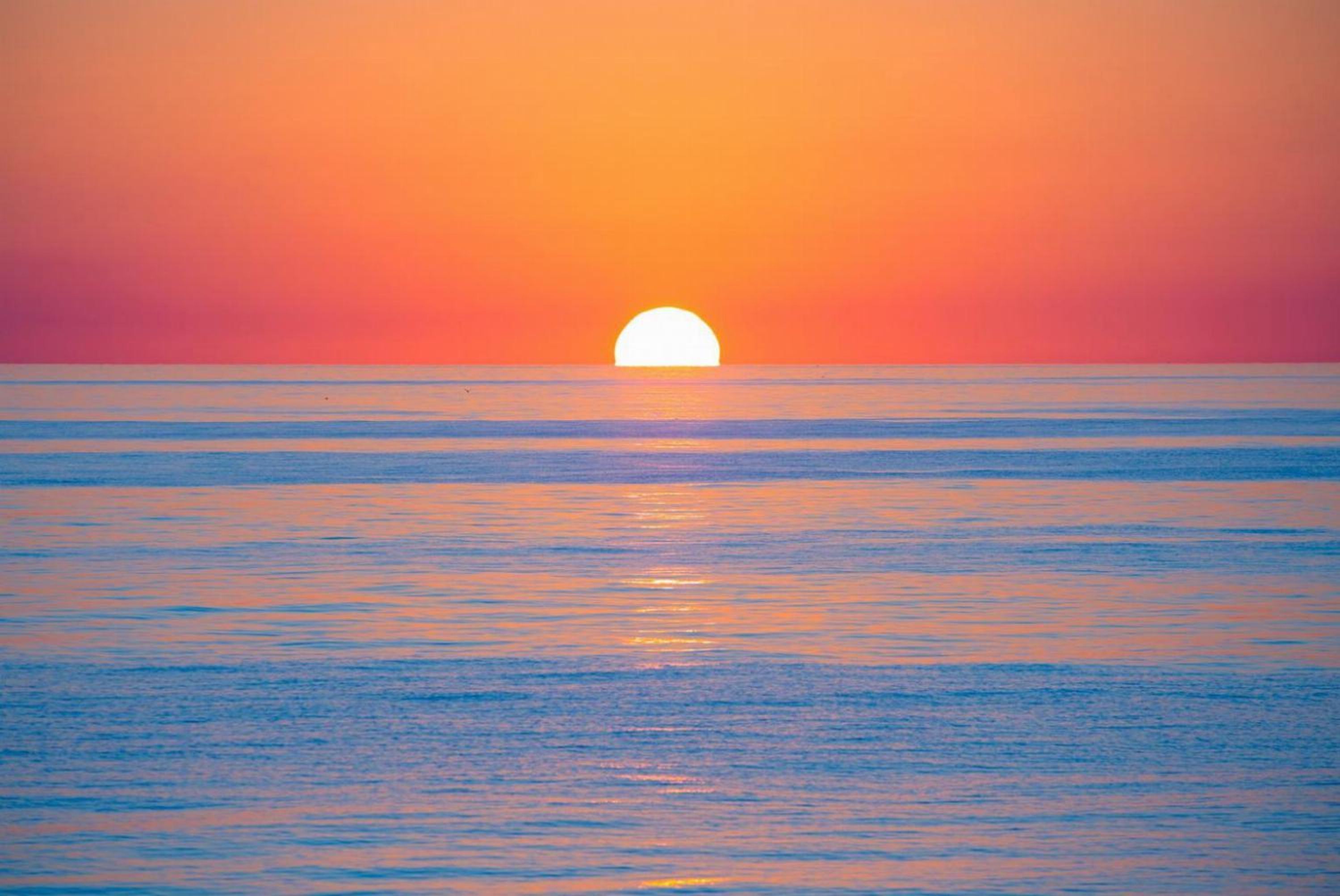 A sunset over a calm sea with a clear horizon.
