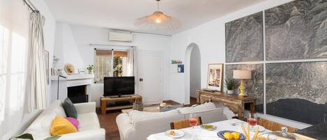 A modern living room with a sofa, dining table, and a TV. There is a fireplace and a dining area with a table set for two.