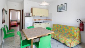 Eine kompakte Küche mit Mikrowelle, Herd und Schränken, ein Esstisch mit Stühlen, eine Couch und ein Feuerlöscher an der Wand.