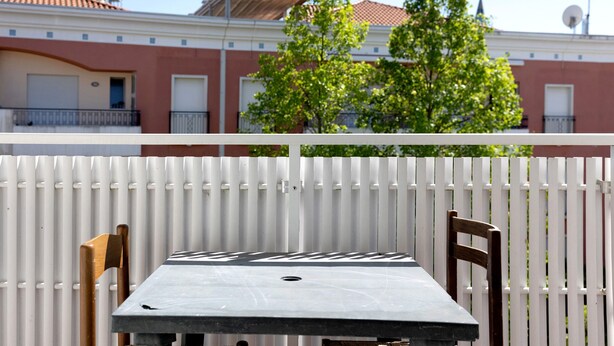Ein Balkon mit weißer Reling, einem Tisch und zwei Holzstühlen.