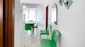 Ein Zimmer mit Esstisch, grünen Stühlen, einer weißen Wand mit Spiegel und einer Holztür.