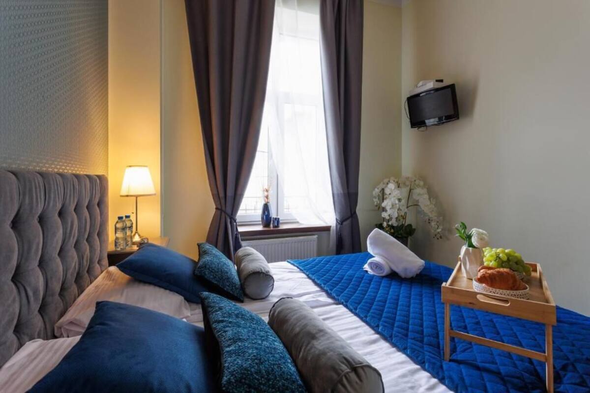 Ein Hotelzimmer mit einem Bett, einem Nachttisch mit Obstschale und einer Flasche, einem an der Wand montierten Fernseher und einem Vorhangfenster.
