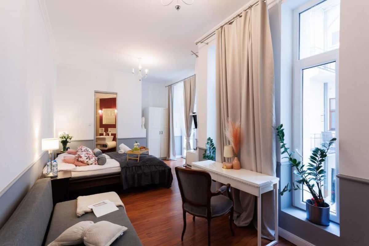 Ein kleines Hotelzimmer mit Bett, Schreibtisch, Stuhl, Nachttisch mit Lampe und einem Fenster mit Vorhängen.