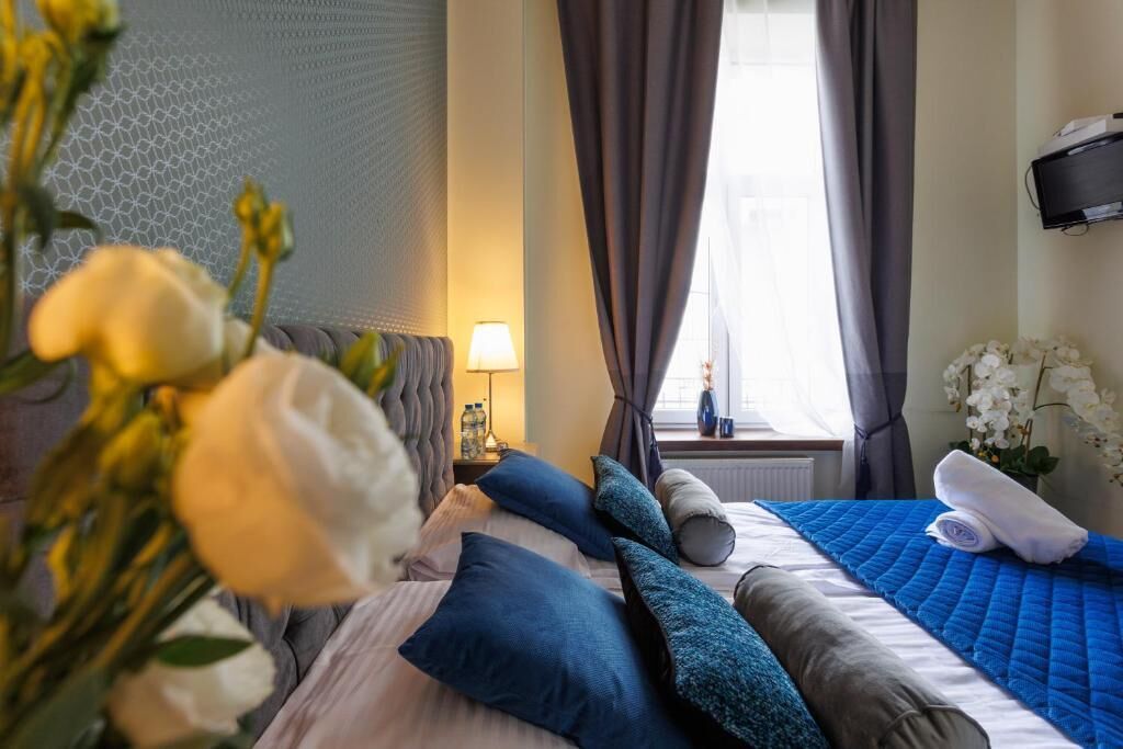 Habitación de hotel con cama, almohadas, lámpara, ventana con cortinas y un florero con flores.