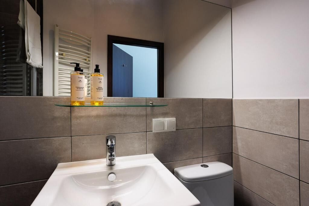 Un baño moderno con un lavamanos blanco, un estante de vidrio con artículos de tocador y un inodoro.