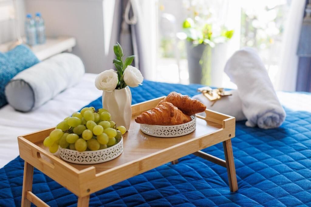 A breakfast tray with grapes and croissants on a bed with a blue quilt.
