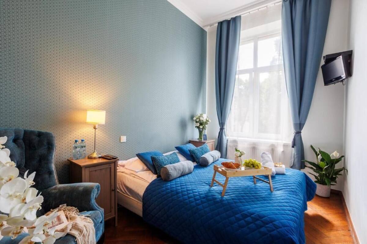 Ein Schlafzimmer mit einer blauen gesteppten Bettdecke, einer Nachttischlampe, einer Ablage mit Früchten und einer Topfpflanze.