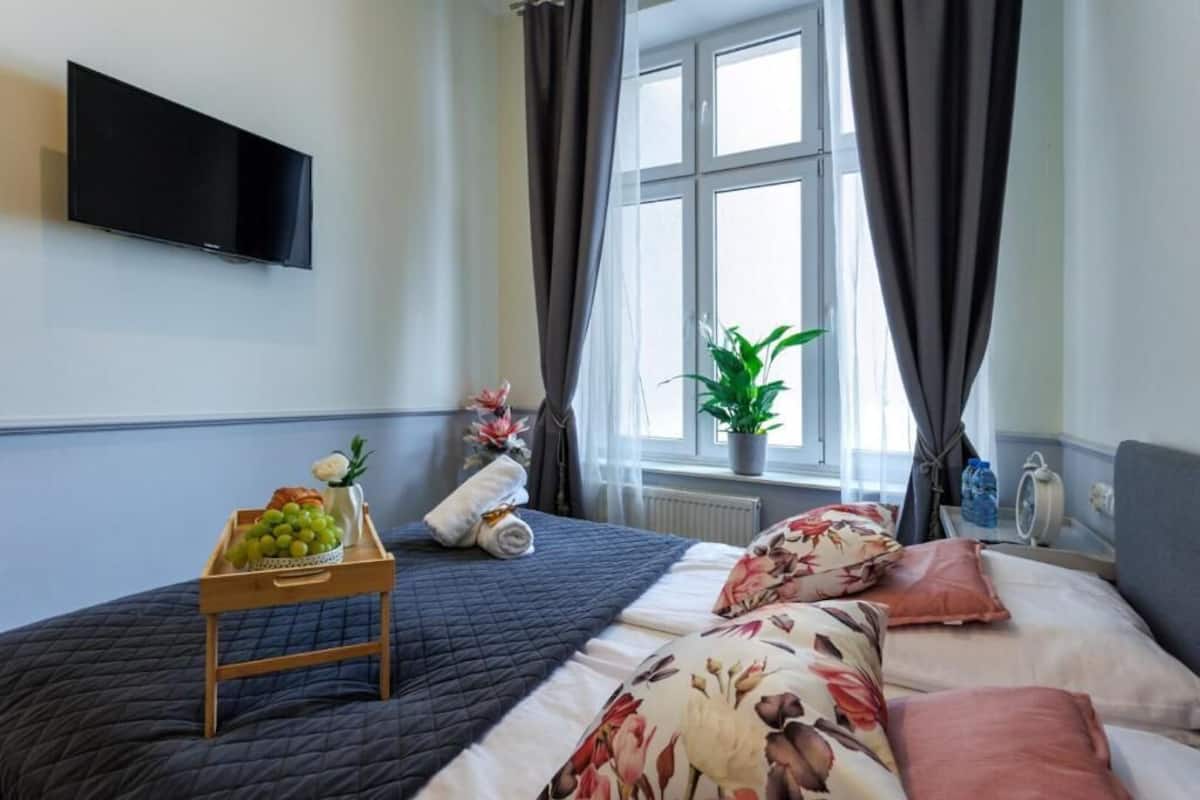 Ein Hotelzimmer mit einem Bett, einem Nachttisch mit Obstkorb, einer Topfpflanze und einem flachbildfernseher an der Wand.