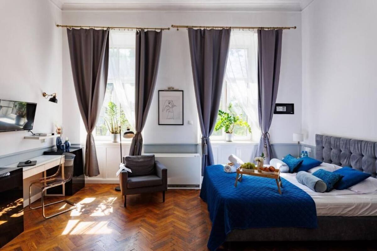Ein modernes Schlafzimmer mit Bett, Schreibtisch, Stuhl und großen Fenstern mit Vorhängen.