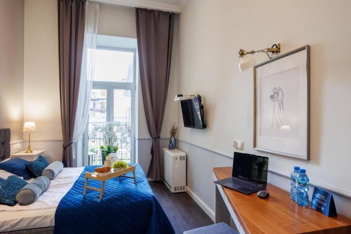 Ein Hotelzimmer mit einem Bett, einem Schreibtisch mit einem Laptop, einem Fernseher und einem Fenster mit Vorhängen.