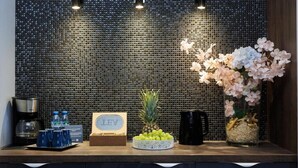 Una zona de recepció amb una paret amb textura, un taulell de fusta, una pinya, un bol de raïm, una gerra negra i un ram de flors.
