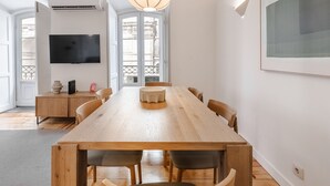 A spacious dining area with a long wooden table, chairs, a modern pendant light, a flat-screen TV, and a large window with a view. - C1 Fully Renovated & Modern | Central | A/C (Lisboa ciudad)