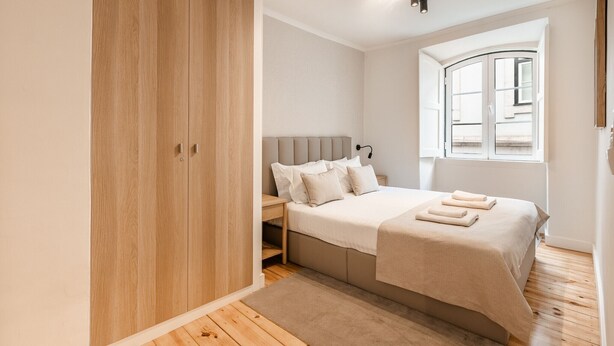 A bedroom with a wooden wardrobe, a bed with a beige bedspread, a nightstand, and a window with a view. - C1 Fully Renovated & Modern | Central | A/C (Lisboa ciudad)
