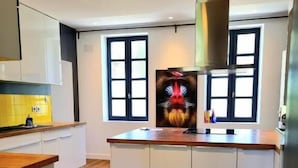 A modern kitchen with white cabinets, a wooden countertop, and a large island. There are two windows with black frames and a painting of a lion's face on the wall. - les granges de jules (Lafitte-Vigordanne)