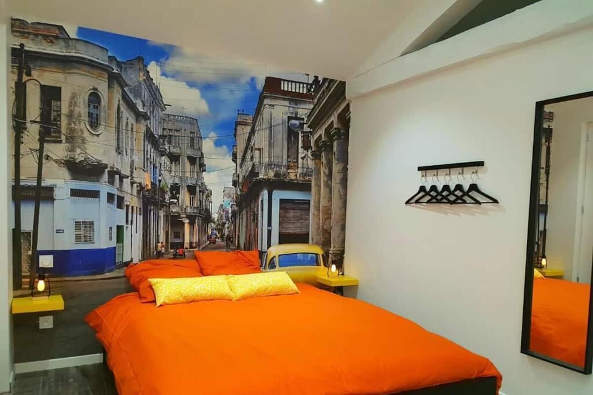 A bedroom with a large bed, a mural of a street scene, a mirror, and a coat rack.