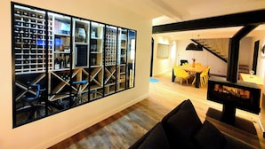 A modern living room with a large wine rack, a dining area with yellow chairs, and a staircase. - les granges de jules (Lafitte-Vigordanne)