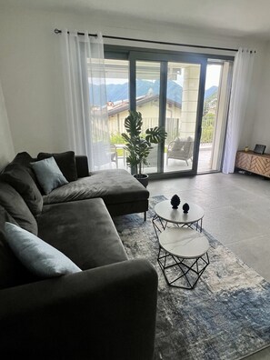 Ein modernes Wohnzimmer mit einem Ecksofa, einem Couchtisch und Blick auf einen Balkon mit Bergblick.