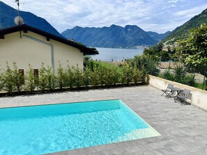 En swimmingpool med en bergskedja i bakgrunden, en byggnad med en satellantenn och utsikt över en sjö och berg.