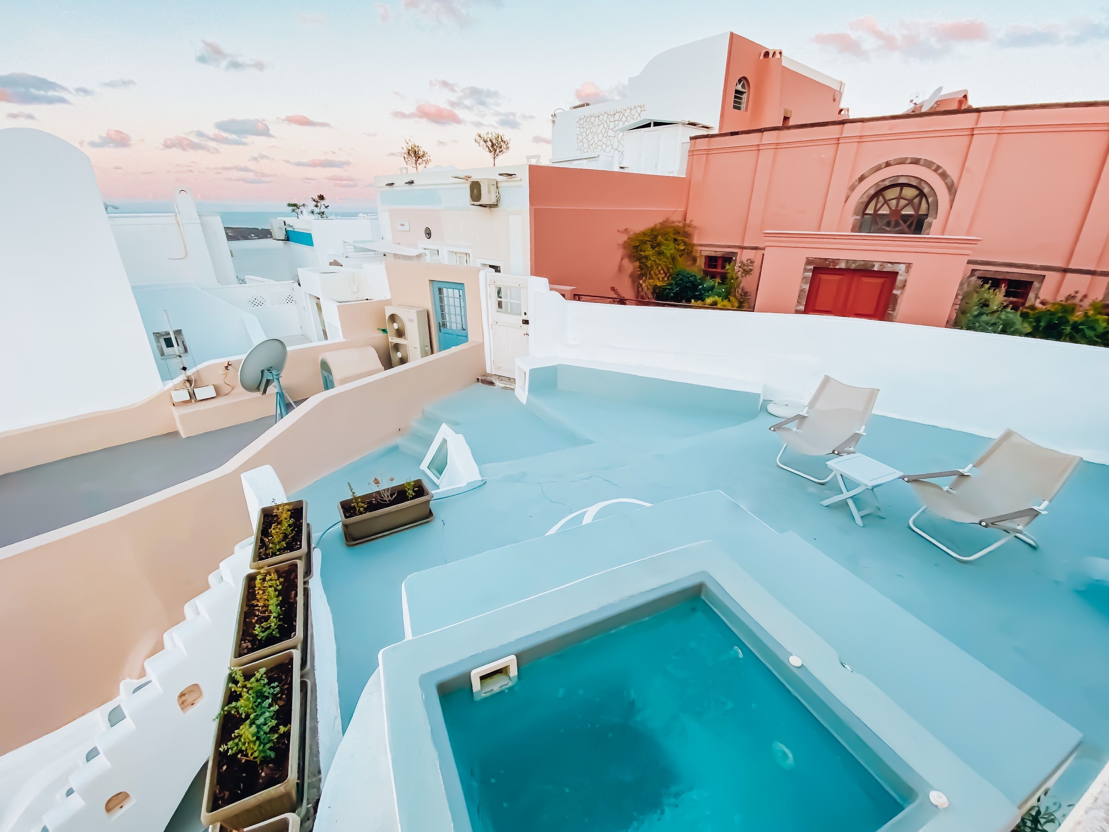 A rooftop pool area with lounge chairs, potted plants, and a view of the cityscape.