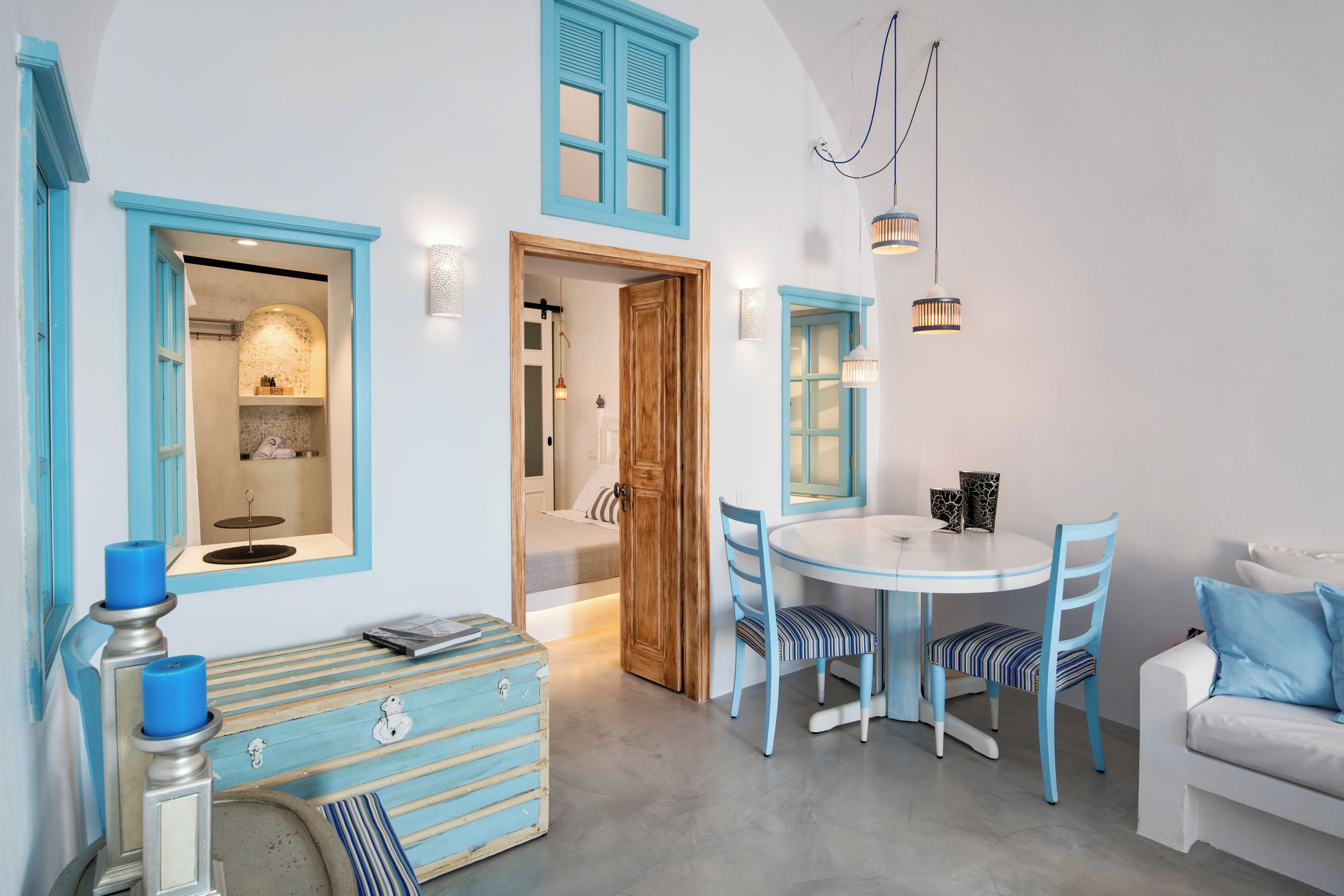A room with a round table, blue chairs, a white sofa, and a wooden door leading to a bathroom.