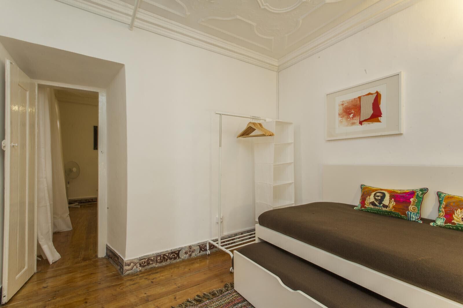 Ein Schlafzimmer mit einem Bett, einem Kleiderschrank, einer Kleiderstange und einem gerahmten Bild an der Wand.