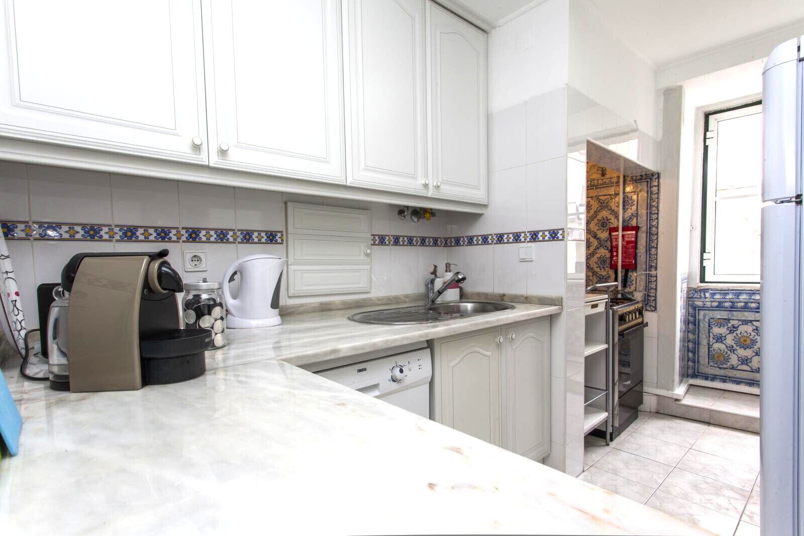 Una cucina compatta con mobili bianchi, un piano di lavoro in marmo e una parete rivestita di piastrelle.