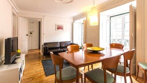 A dining area with a wooden table and chairs, a television on a stand, a black leather sofa, and a painting on the wall. - C2 Authentic Stay | XVIII Century Charm | DT (Lisboa ciudad)
