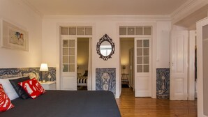A bedroom with a large bed, a nightstand, a mirror, and a door leading to another room. - C2 Authentic Stay | XVIII Century Charm | DT (Lisboa ciudad)