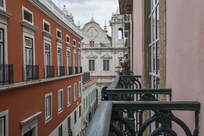 A narrow street with buildings on either side, featuring balconies with wrought iron railings and a prominent white building with a dome and cross. - C2 Authentic Stay | XVIII Century Charm | DT (Lisboa ciudad)