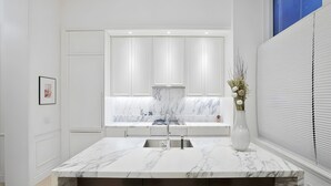 Een moderne keuken met witte kasten, een marmeren aanrechtblad en een inbouwspoelbak.